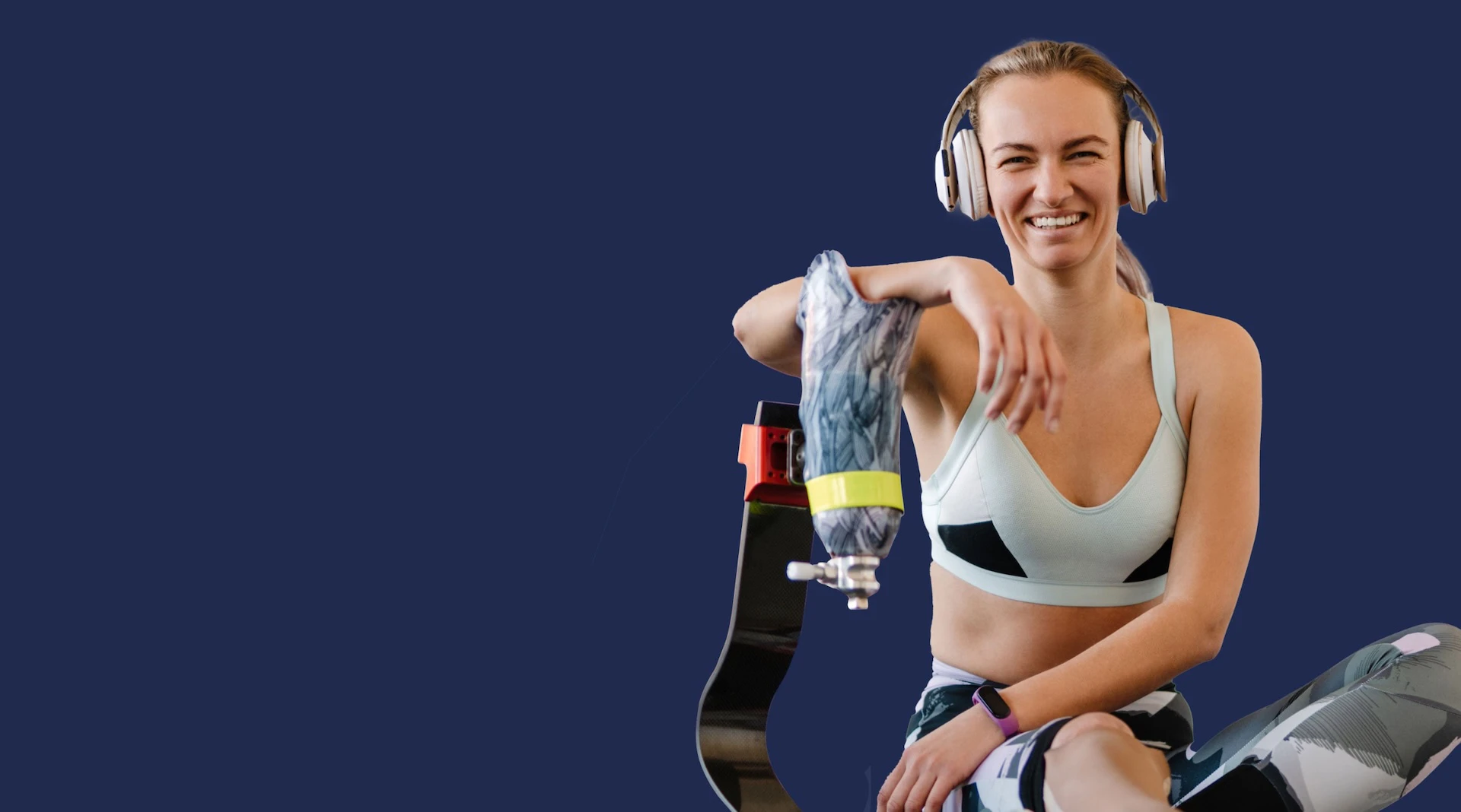 Smiling woman with a prosthetic leg wearing athletic gear and headphones, seated against a dark blue background.
