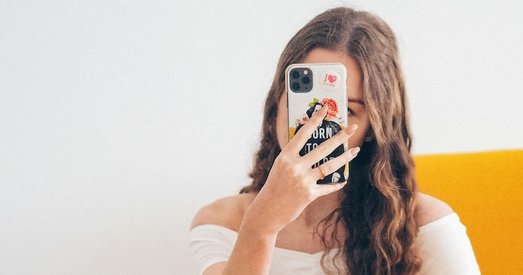 Young woman in a white top takes a selfie with a decorated phone, representing a social media influencer.