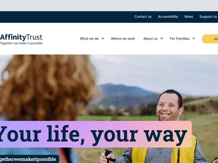 A man with Down’s syndrome smiles as he walks outdoors using walking poles, looking towards a woman in the foreground. A banner over the image reads: “Your life, your way”.