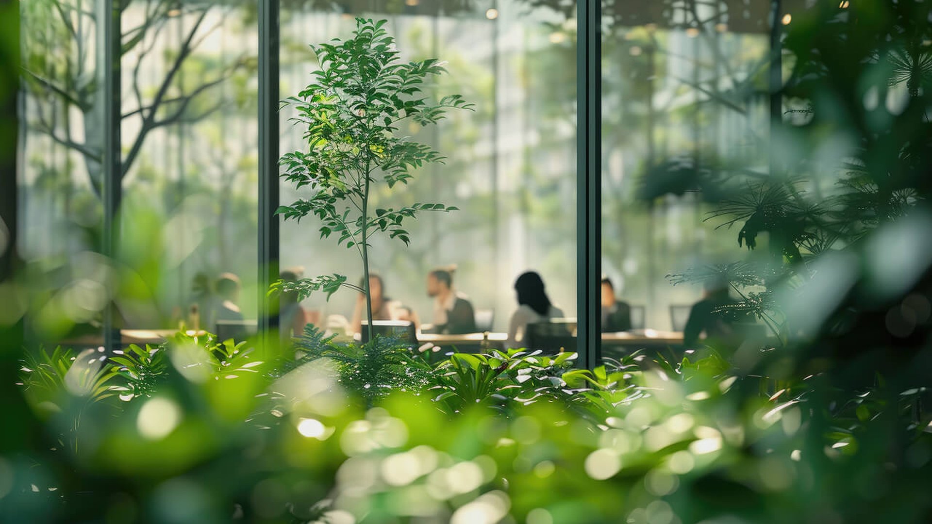 A modern office meeting room viewed through a window surrounded by lush green plants, with people in discussion inside, reflecting a sustainable and nature-integrated workplace.