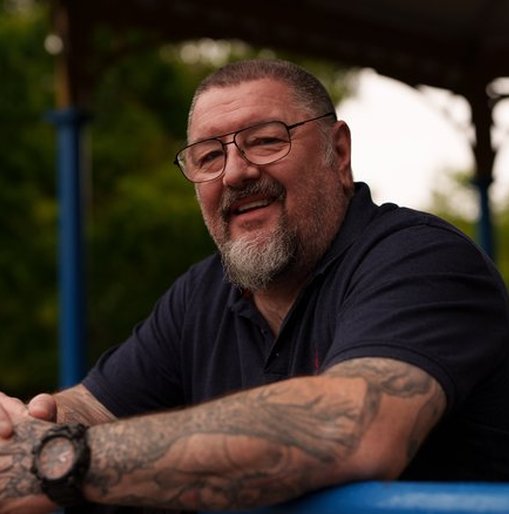 Bryn, a veteran supported by Walking With The Wounded (WWTW), smiling as he leans on a blue railing in a park setting.