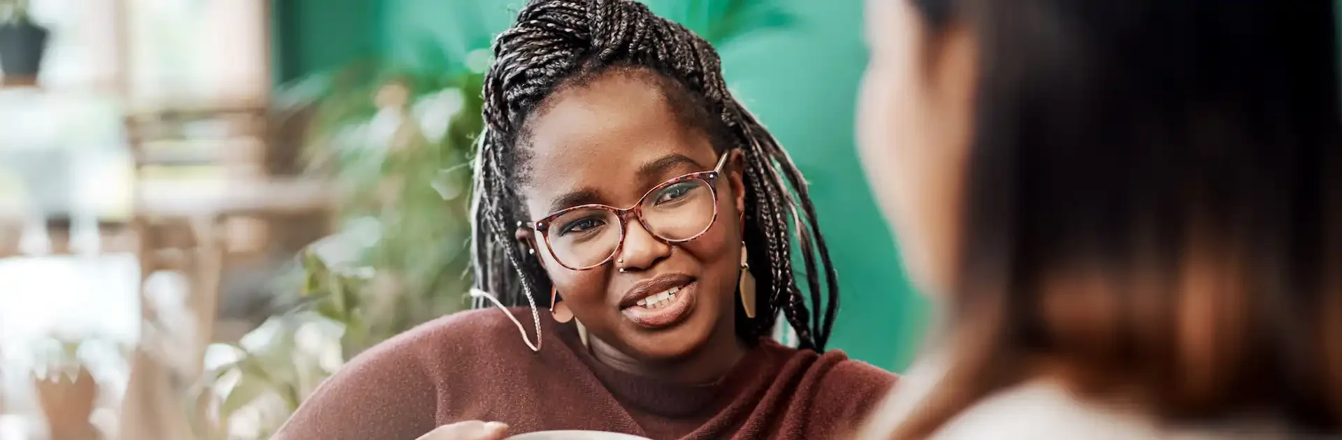 Two women sitting together and talking over mugs of tea or coffee, with one woman smiling warmly and actively engaging in the conversation in a cozy, indoor setting.