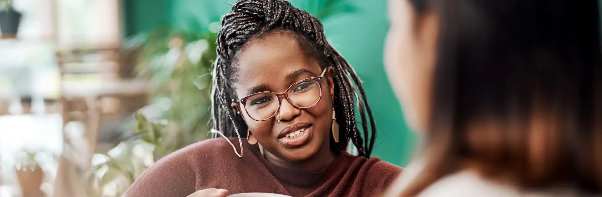Two women sitting together and talking over mugs of tea or coffee, with one woman smiling warmly and actively engaging in the conversation in a cozy, indoor setting.