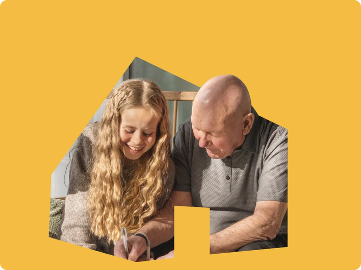 Smiling young girl and elderly man sitting together on a bench, writing or drawing in a notebook with natural sunlight streaming in.