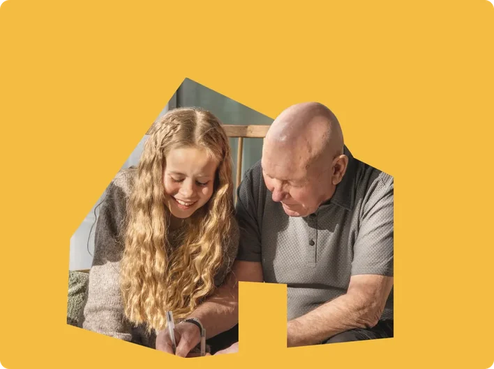 Smiling young girl and elderly man sitting together on a bench, writing or drawing in a notebook with natural sunlight streaming in.