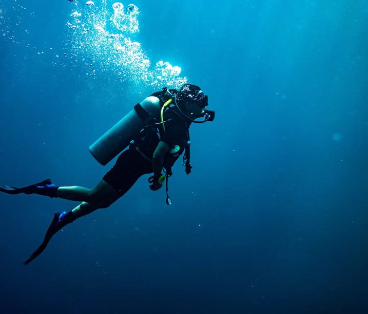 Scuba diver in full gear swimming underwater in deep blue ocean, surrounded by air bubbles and ambient light.