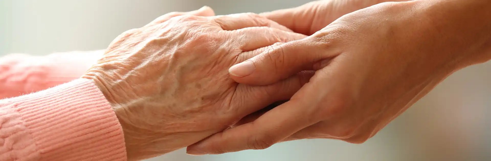 Close-up of a younger person gently holding the hands of an older person, symbolising care, compassion, and support.