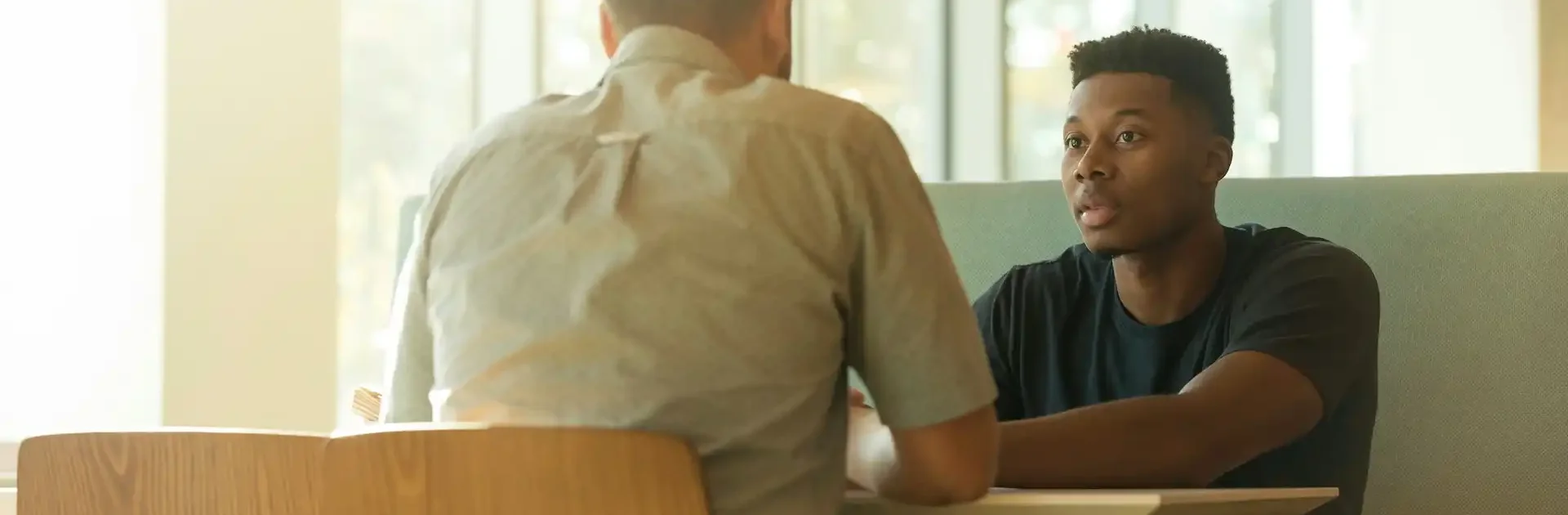Two men sitting across from each other in a bright, modern setting, engaged in a serious and focused conversation.