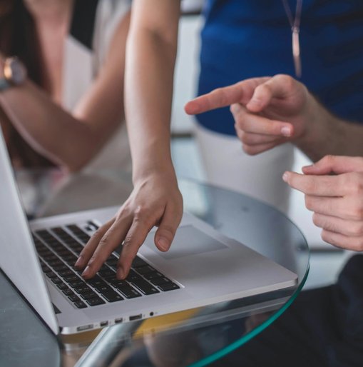 Close-up of three people collaborating around a laptop, with one person typing and another pointing at the screen during a web accessibility review or design discussion.
