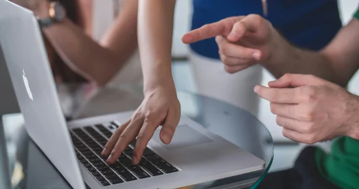 Close-up of three people collaborating around a laptop, with one person typing and another pointing at the screen during a web accessibility review or design discussion.
