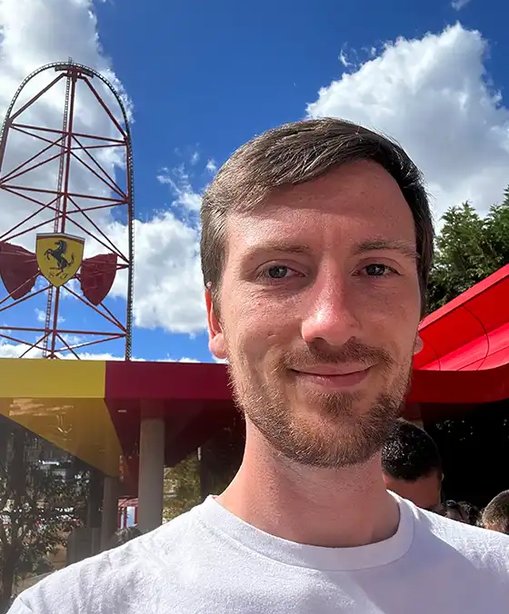 Tom taking a selfie outside, smiling beneath a blue sky with scattered clouds.
