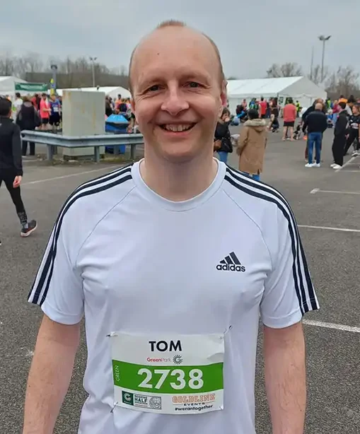 Tom smiling after a run, wearing a race number and white running shirt at a large outdoor running event.