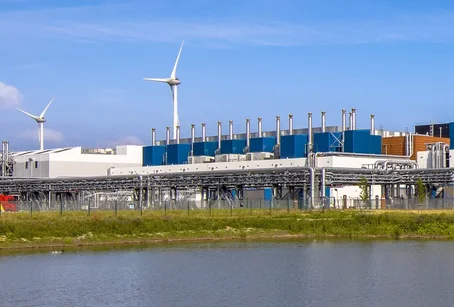 A large industrial data centre with wind turbines in the background, reflecting efforts toward renewable energy and sustainable infrastructure.