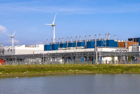 A large industrial data centre with wind turbines in the background, reflecting efforts toward renewable energy and sustainable infrastructure.