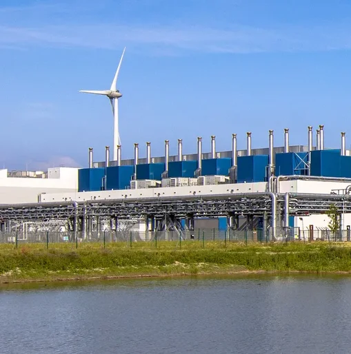 A large industrial data centre with wind turbines in the background, reflecting efforts toward renewable energy and sustainable infrastructure.