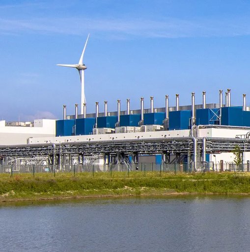 A large industrial data centre with wind turbines in the background, reflecting efforts toward renewable energy and sustainable infrastructure.