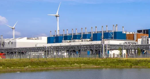 A large industrial data centre with wind turbines in the background, reflecting efforts toward renewable energy and sustainable infrastructure.