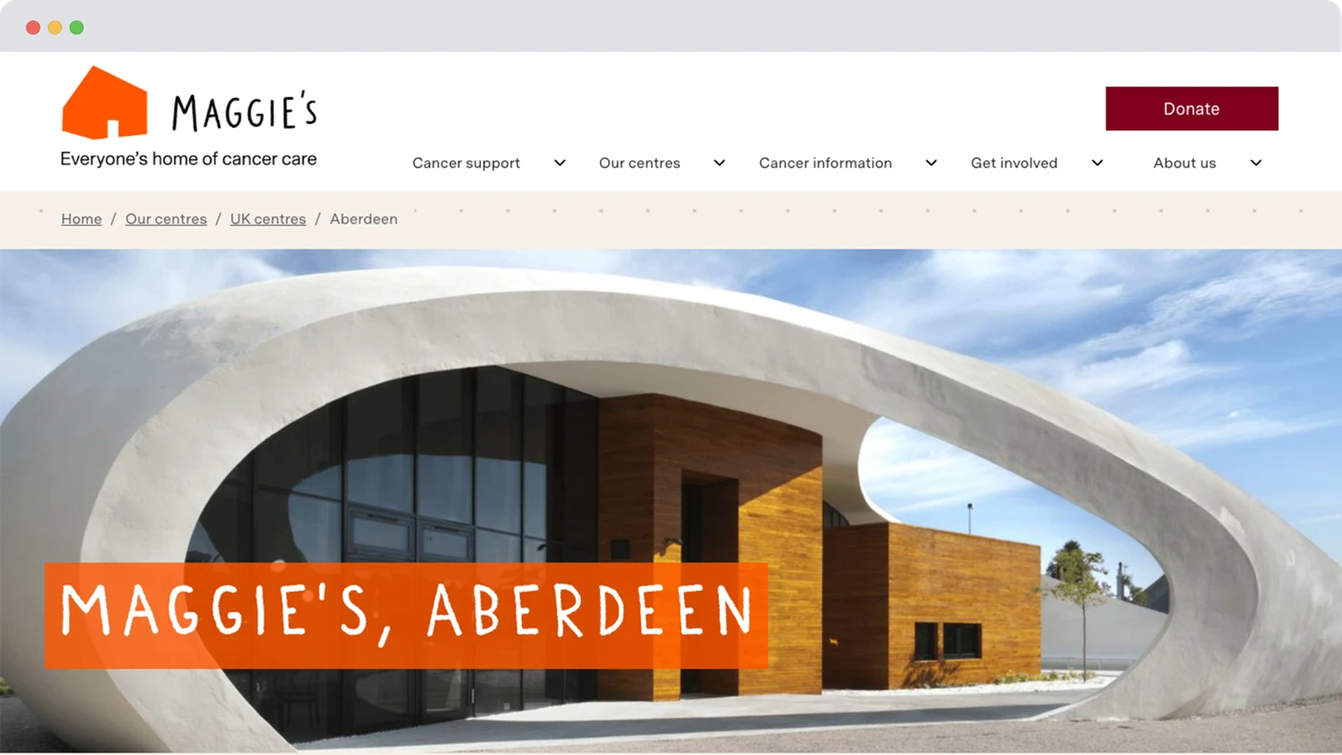 Homepage of Maggie’s Centre Aberdeen showing the iconic curved white architecture with wooden accents, under clear skies. Navigation menus appear above with a red donate button.