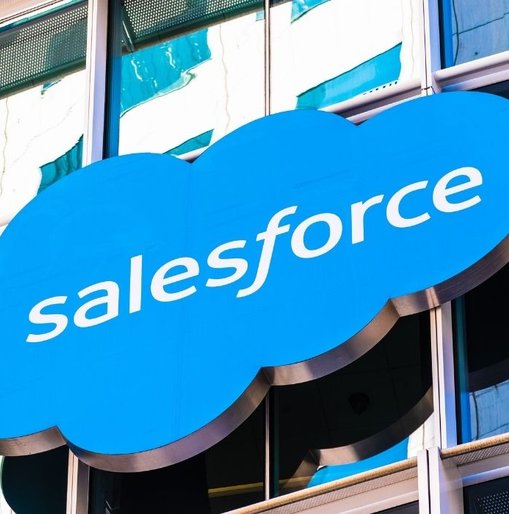 Close-up of a Salesforce logo on a blue cloud-shaped sign outside a modern glass office building.
