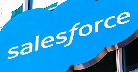 Close-up of a Salesforce logo on a blue cloud-shaped sign outside a modern glass office building.