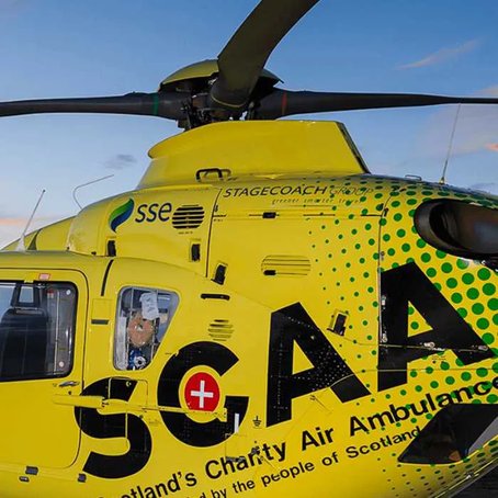 Close-up of a bright yellow Scotland’s Charity Air Ambulance helicopter with visible logos and markings, captured against a clear blue sky.