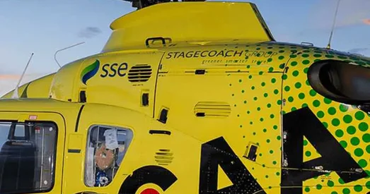 Close-up of a bright yellow Scotland’s Charity Air Ambulance helicopter with visible logos and markings, captured against a clear blue sky.